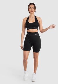 Czarny sportowy zestaw składający się z topu na ramiączkach i szortów z wysokim stanem. Materiał jest gładki, dopasowany, z elastycznymi taśmami z logo.