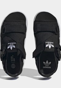 Black Adidas sandals with adjustable straps, white logo tags, and insoles labeled "END PLASTIC WASTE" and Adidas trefoil logo.