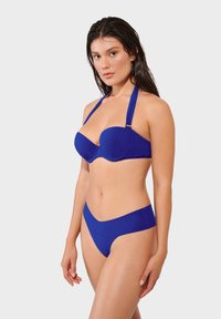 Bikini s visokim strukom u jednobojnom plavom materijalu. Gornji dio ima strukturirani, podstavljen dizajn s podesivim halter trakama i zlatnim detaljem.