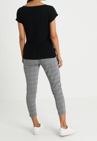 Camiseta negra de manga corta y pantalones tapered de cuadro de gallo grises, combinados con zapatillas blancas, vistos desde atrás.
