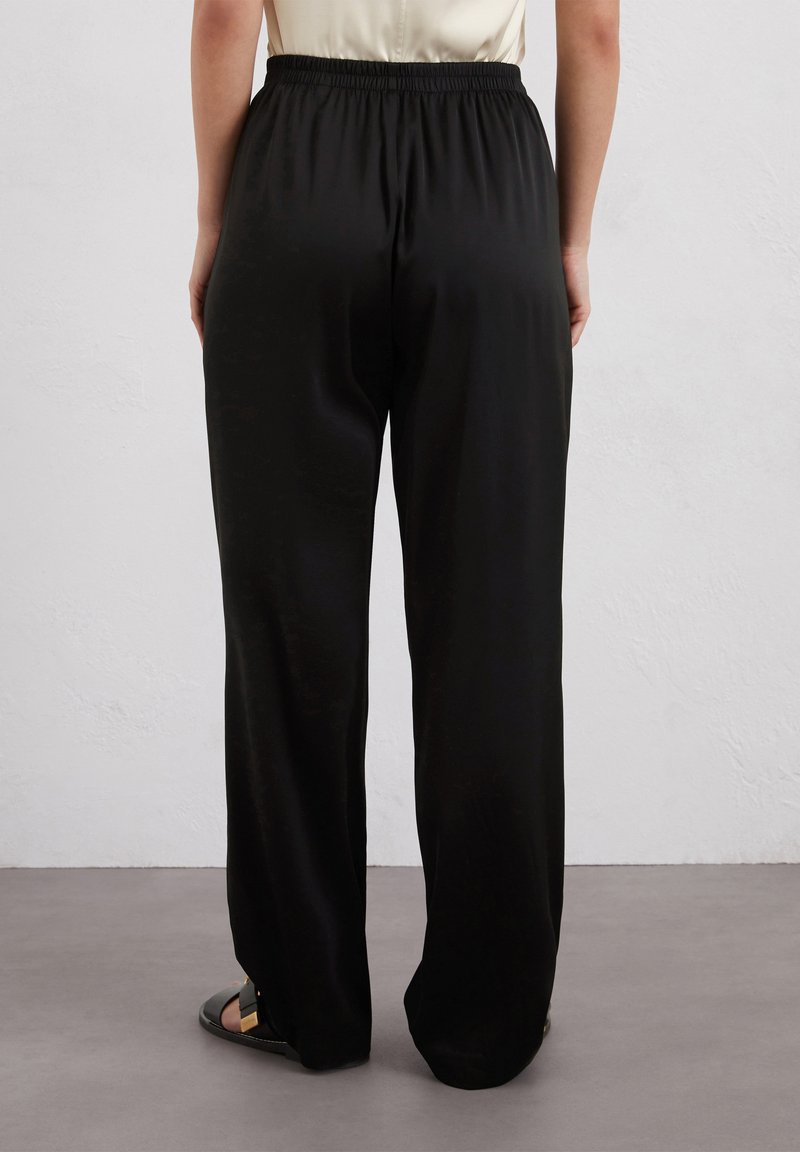 Czarne spodnie o szerokich nogawkach z elastycznym pasem, wykonane z gładkiego materiału. Charakteryzują się luźnym krojem i minimalną ilością szwów, odpowiednie na co dzień.