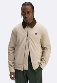 Giacca beige con cerniera, colletto in velluto a coste marrone, texture trapuntata e logo ricamato sul petto. Caratterizzata da tasche laterali e vestibilità comoda.