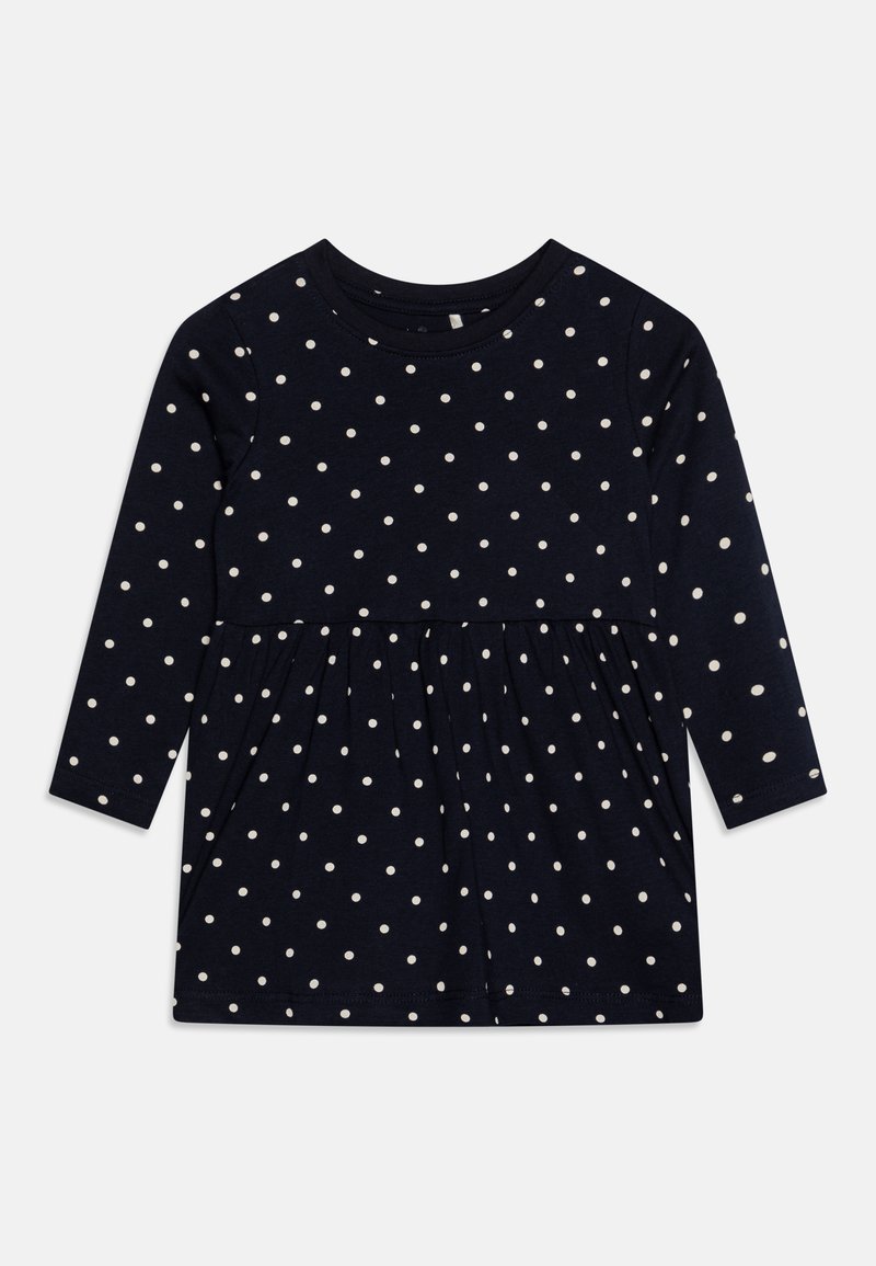 Jūros mėlynos suknelės ilgomis rankovėmis, baltais taškeliais, apvaliu iškirpimu ir surinktomis sijono detalėmis. Pagaminta iš švelnios, elastingos medžiagos.