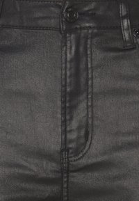 Svarta denimjeans med en mjuk textur, väldefinierade sömmar och en vanlig knappknäppning. Tyget har en lätt glans.