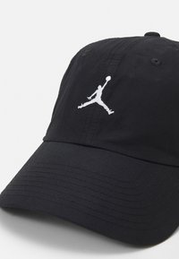 Cappello nero in cotone con visiera curva. Presenta un logo Jumpman ricamato in bianco sulla parte frontale e dettagli di cucitura sulla corona.