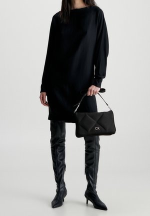 Zwarte jurk met lange mouwen, tot op de knie, gecombineerd met hoge glanzende zwarte leren laarzen. Zwarte gewatteerde handtas met zilverkleurige details en logo.