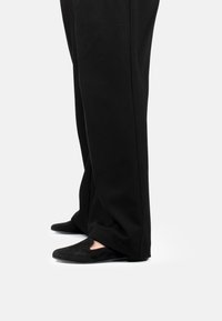 Scarpe in suede nere con un leggero design a ritaglio sulla parte anteriore, abbinate a pantaloni neri a gamba larga, viste di lato.