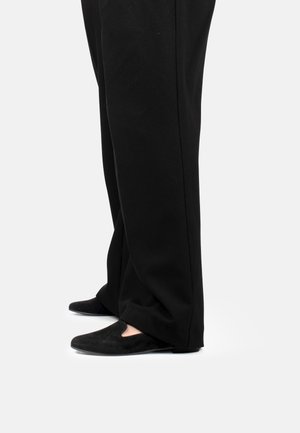 Scarpe in suede nere con un leggero design a ritaglio sulla parte anteriore, abbinate a pantaloni neri a gamba larga, viste di lato.