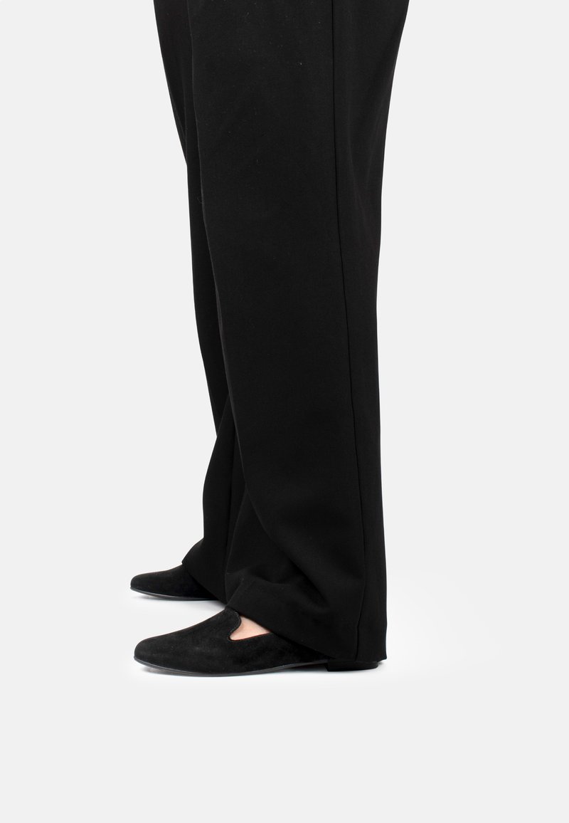 Scarpe in suede nere con un leggero design a ritaglio sulla parte anteriore, abbinate a pantaloni neri a gamba larga, viste di lato.