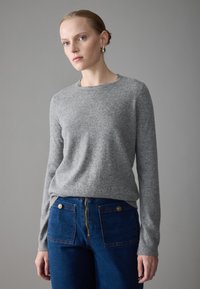 Gray wool blend sweater with long sleeves and a crew neck, paired with blue denim pants featuring a mid-rise zipper and back pockets.