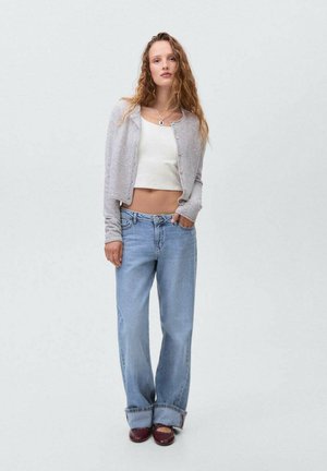 Světle šedý pletený kardigan přes bílý crop top, v kombinaci s volně střiženými modrými džíny a hnědými botami. Jednoduchý design s ležérním stylem.
