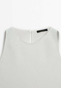 Top bianco senza maniche con scollo rotondo e una leggera texture. Presenta una chiusura a chiave sul retro con un singolo bottone e un'etichetta visibile.