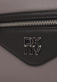 Svart og mørkegrå lærveske med en sølvglidelås og et DKNY-logo i et geometrisk design på frontpanelet.
