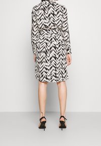 Black and white zigzag-patterned dress with long sleeves, a collar, and a tied waist. Fabric is smooth, designed to hit mid-thigh.