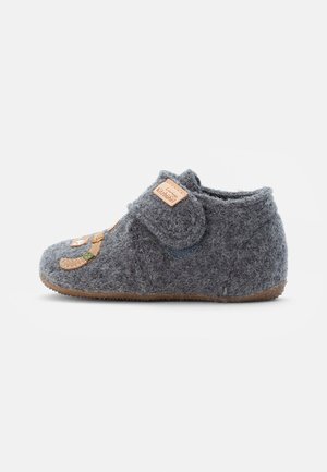 Pantofole grigie in feltro con fibbia in Velcro, etichetta in pelle e design ricamato che presenta un volto sorridente e elementi decorativi.