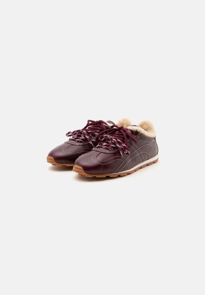 Paire de baskets en cuir rouge foncé avec coutures blanches, lacets à motifs, semelles marron clair et doublure en fausse fourrure beige à l'intérieur.