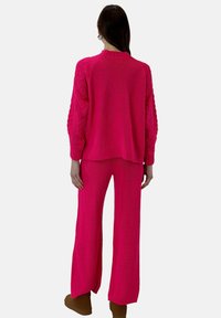 Różowy komplet swetra i spodni z dzianiny z fakturowanymi rękawami w warkocz, luźny krój i ściągacze. Brak dodatkowych detali lub wzorów.