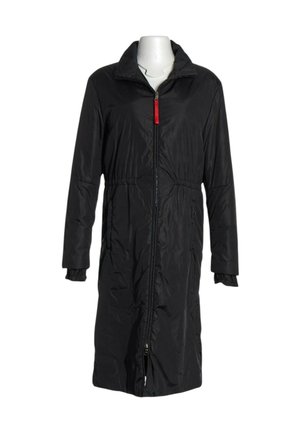 Manteau long rembourré noir avec fermeture éclair frontale et languette rouge, doté d'un col et de poignets élastiqués sur un mannequin blanc.