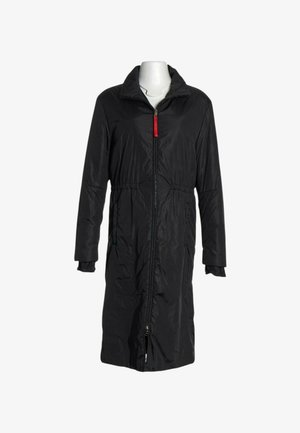 Manteau long rembourré noir avec fermeture éclair frontale et languette rouge, doté d'un col et de poignets élastiqués sur un mannequin blanc.
