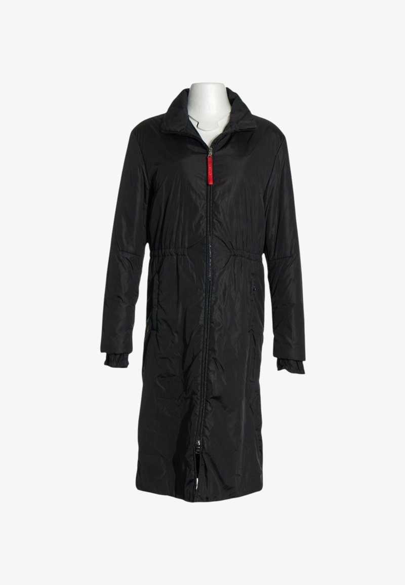 Manteau long rembourré noir avec fermeture éclair frontale et languette rouge, doté d'un col et de poignets élastiqués sur un mannequin blanc.