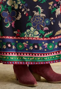 Tumedast sinise lillemustriga kangas, mis sisaldab elavaid lilli ja liblikaid. Pitsitud äär on kaunistatud mitmevärviliste ribade ja loomamotiividega. Burdeaux värvi nahast saapad.