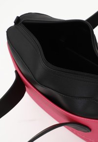 Borsa bicolore nera e rosa con chiusura a zip; presenta una texture liscia e un manico singolo per il trasporto. L'interno è spazioso e non foderato.