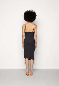 Černé šaty bez rukávů s přiléhavým střihem, délky do poloviny lýtek, se rozparkem na jedné straně. Kombinované s oranžovými sandály.