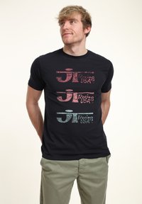 Schwarzes T-Shirt mit kurzen Ärmeln, das drei gestapelte Logos in verschiedenen Farben zeigt: rot, pink und türkis, mit dem Text "Racing USA" in einer fetten Schriftart.