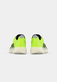 Zapatillas verdes brillantes con rayas negras, de textura suave y suela de goma ligera. El talón presenta un acento gris y forro suave.
