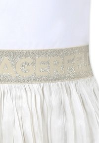 Jupe plissée blanche avec une taille en paillettes argentées portant l'inscription "LAGERFELD" en beige clair, mettant en valeur une finition texturée.