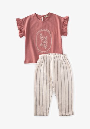 Rozā īsām piedurknēm blūze ar rufu piedurknēm, ar baltu ziedu grafiku. Svītrainas, vieglas krēmkrāsas bikses ar elastīgu jostas vietu.