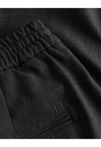 Czarne dresy z tkaniny o fakturze jodełki, z elastycznym pasem i minimalistycznym detalem kieszeni z subtelnym przeszyciem.