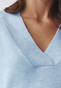 Pull en tricot bleu clair avec un col en V profond, une texture subtile et des accents côtelés sur le col et l'ourlet.