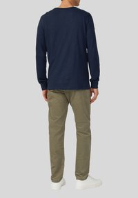 Felpa navy a maniche lunghe con collo a girocollo, maniche aderenti, abbinata a pantaloni verde oliva e sneakers bianche. Design semplice e monocromatico.