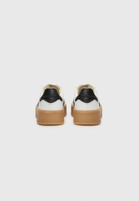 Weiße Sneakers mit schwarzen Akzenten und einer sandfarbenen Sohle, die ein strukturiertes Design und eine erhöhte Ferse aufweisen, und einen minimalistischen und modernen Eindruck vermitteln.