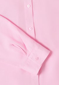 Chemise rose clair à manches longues avec poignets boutonnés et boutons sur le devant, montrant la texture détaillée du tissu et les coutures.