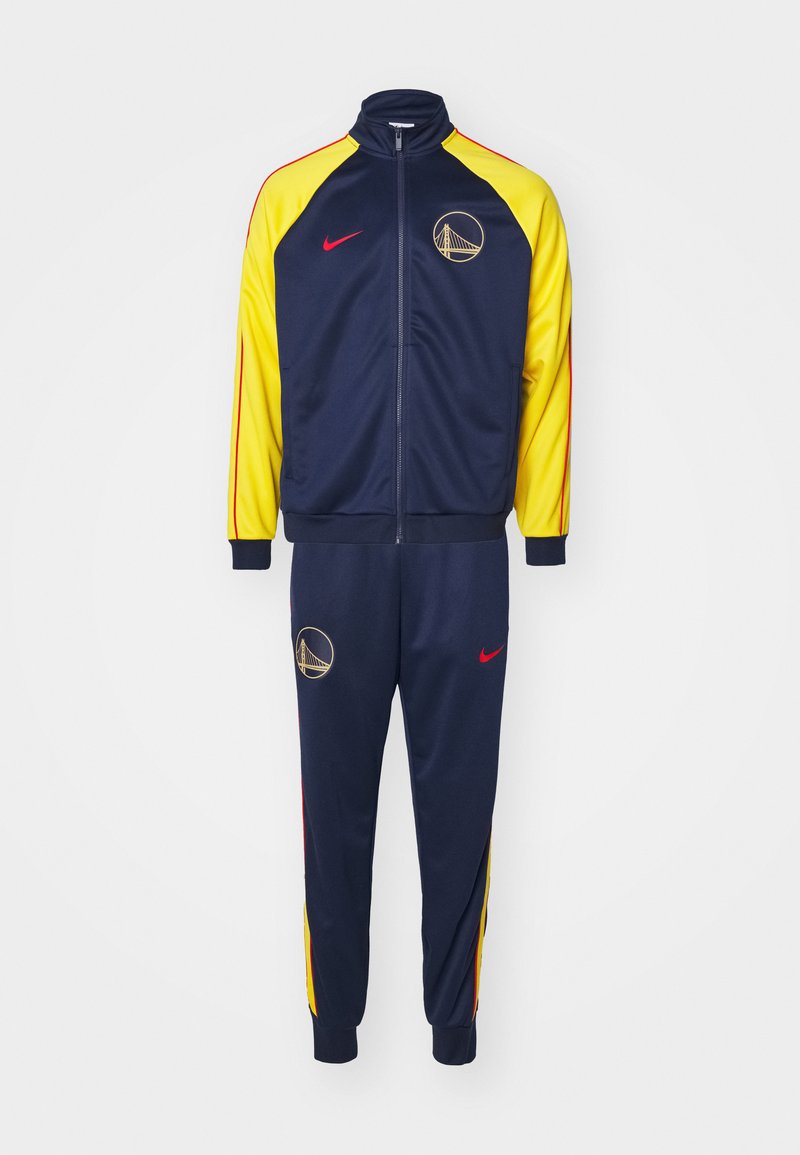 Tuta navy e gialla con giacca con zip, colletto a costine, dettagli rossi e logo; pantaloni abbinati con orli e dettagli del logo.