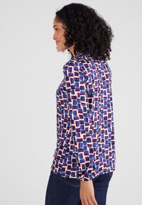 Maglia a maniche lunghe in blu, rosso e crema con un motivo geometrico. Tessuto morbido, vestibilità comoda e scollatura rotonda.