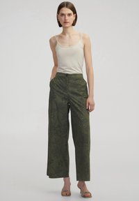 Pantalones de pierna ancha verde oliva con bordados florales y adornos; combinados con una camiseta ajustada beige y sandalias ligeras.