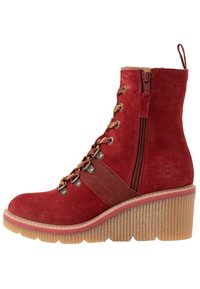 Red suede ankle boot with a ribbed sole, contrasting brown leather strap, gold eyelets, and a side zipper for easy wear. Heightened heel design.