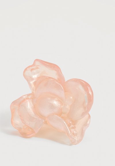 Διαφανές πλαστικό κλιπ μαλλιών σε ροδακινί-ροζ χρώμα με κυματιστές άκρες σε σχήμα πέταλου, πάνω σε λευκό φόντο.