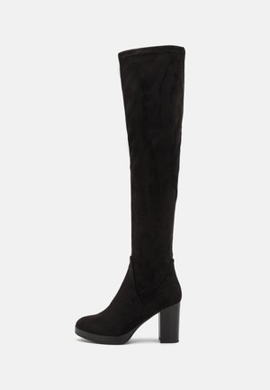 Botte hauteur genou en daim noir avec bout arrondi et talon haut épais sur fond blanc.