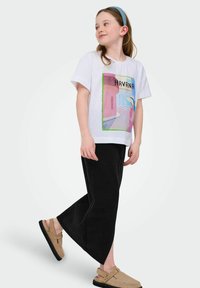 Bijela majica s šarenim grafičkim dizajnom "Havana", uparena s crnim dugim hlačama i bež slip-on cipelama. Jednostavan, ležeran outfit.