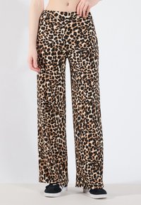 Leopardprint wijde pijpen broek van zachte stof, met een soepele tailleband en zwarte accenten aan de zoom, gestyled met zwarte sneakers.