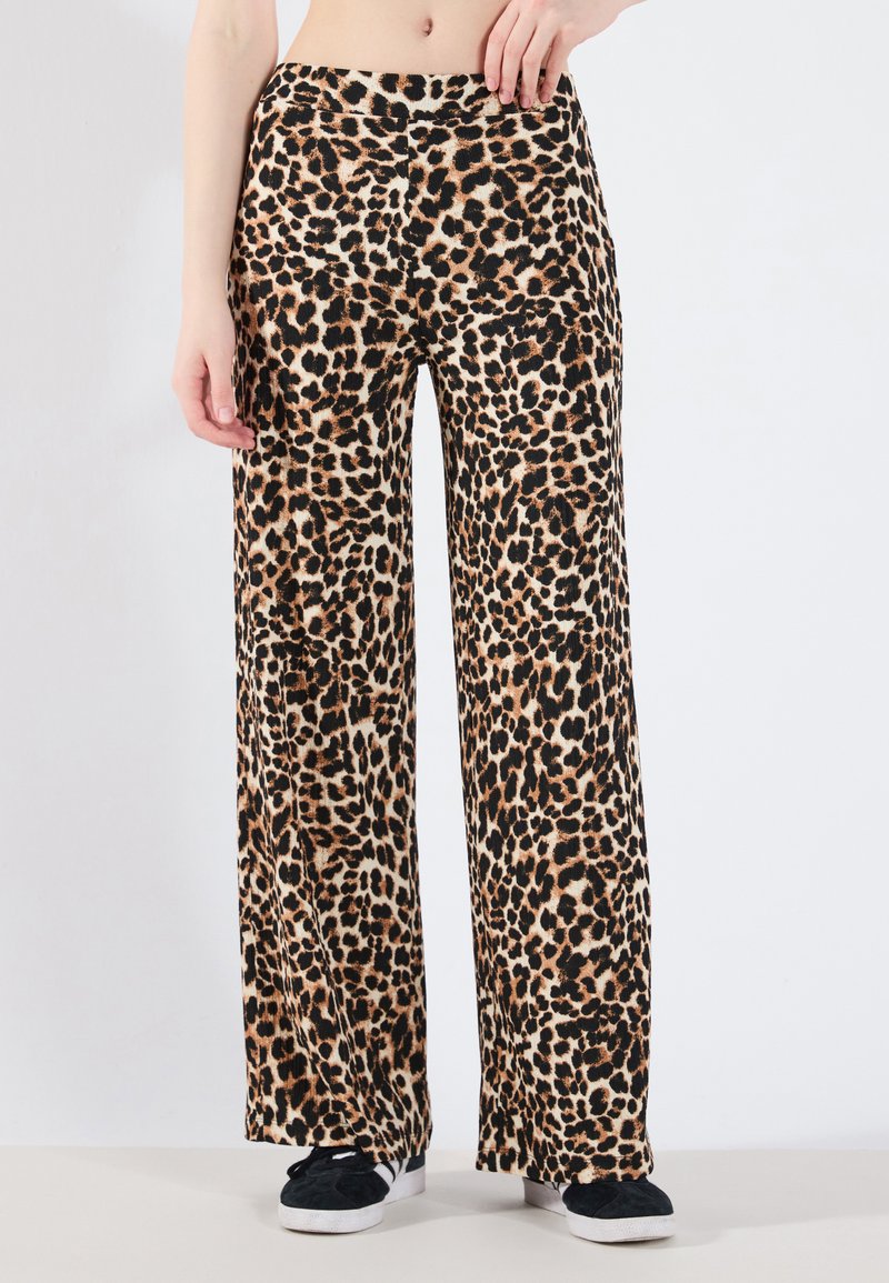 Leopardprint wijde pijpen broek van zachte stof, met een soepele tailleband en zwarte accenten aan de zoom, gestyled met zwarte sneakers.