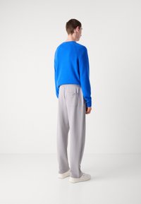 Suéter de punto azul y pantalones grises con cintura elástica, mostrados desde atrás. El suéter tiene acentos acanalados; los pantalones cuentan con un bolsillo lateral y un corte holgado.