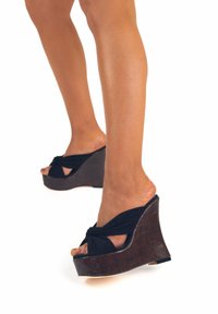 Sandali con zeppa, upper in tessuto nero caratterizzato da un design annodato e una suola in pianta di legno scuro. Texture liscia e retro aperto.