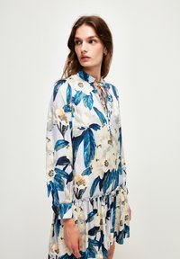 Blumenkleid mit großen blauen und weißen Blumen, langen Ärmeln und einem gerafften Saum. Hergestellt aus leichtem Stoff mit sanftem Glanz.