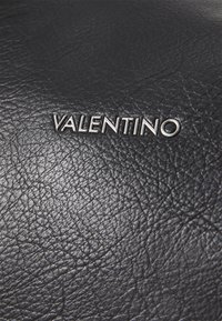 Black leather surface with a textured finish, featuring a silver "VALENTINO" logo in a modern font.