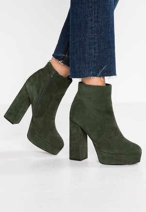 Botines de ante verde con un alto tacón de bloque y plataforma, que presentan un cierre lateral y detalles de costura mínimos.